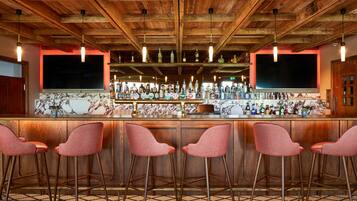 A bar area with wooden ceiling beams, a marble countertop, and four pink bar stools.