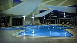 An indoor swimming pool with multiple lanes, lounge chairs, and a large glass wall. - The K Club (Straffan)