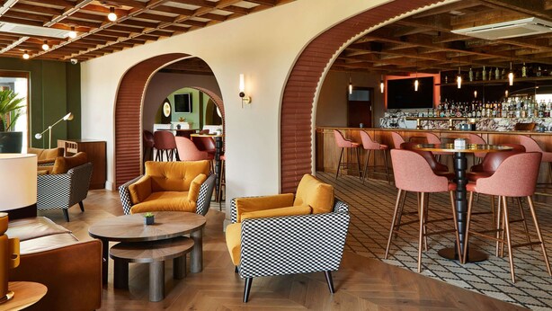 A bar area with round tables and chairs, a bar counter with bottles, and a seating area with sofas and chairs. - The K Club (Straffan)