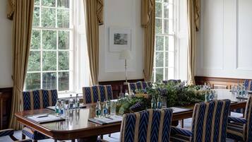 Un salón de conferencias con una mesa larga, sillas de estampado azul y un centro de mesa floral.