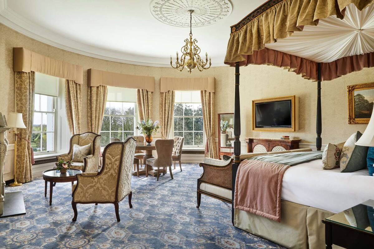 A luxurious bedroom with a four-poster bed, a chandelier, and a large window with curtains.