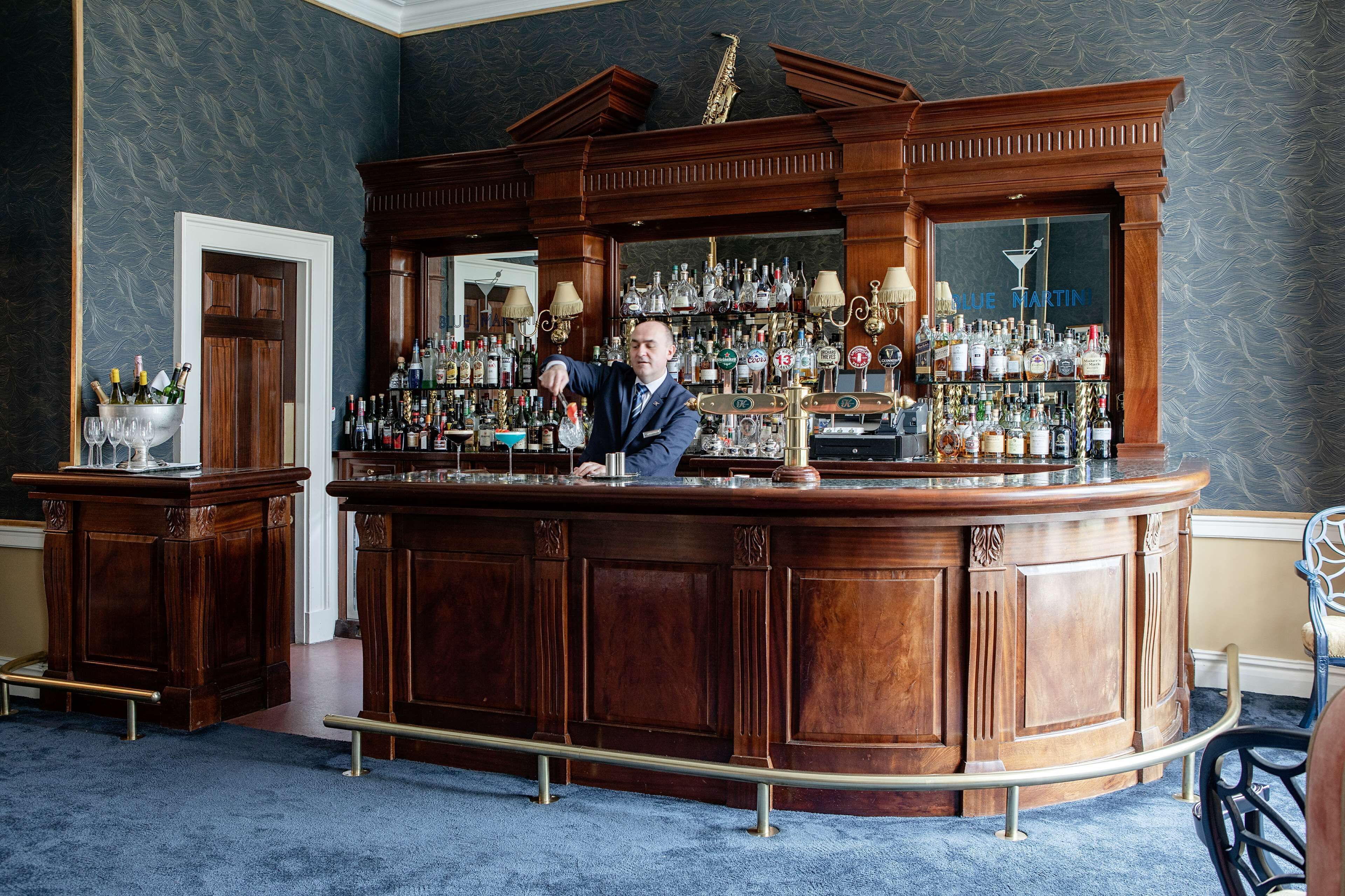 A bar area with a wooden counter, shelves of bottles, and a large mirror.