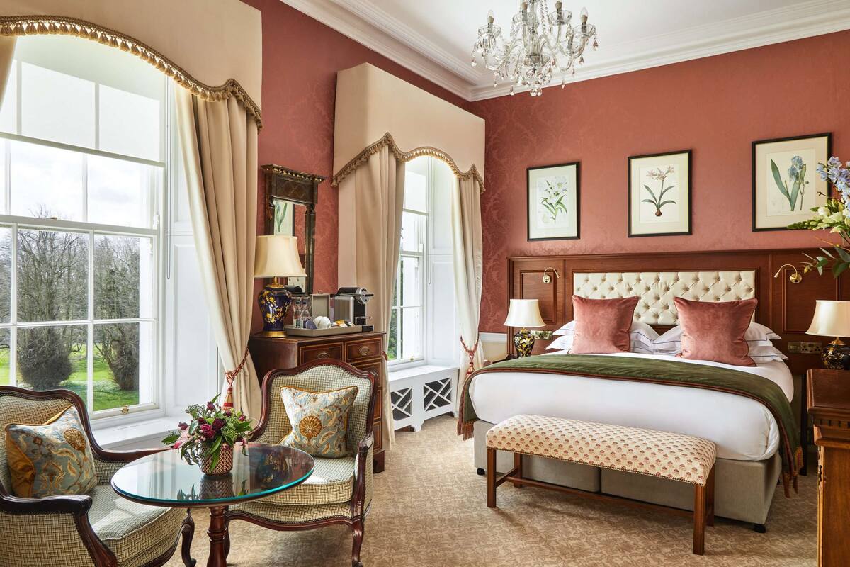 A spacious bedroom with a large bed, a sitting area with a glass table, and a view of the outdoors.