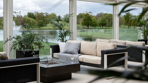 A modern outdoor seating area with a sofa, a fire pit, and potted plants. - The K Club (Straffan)