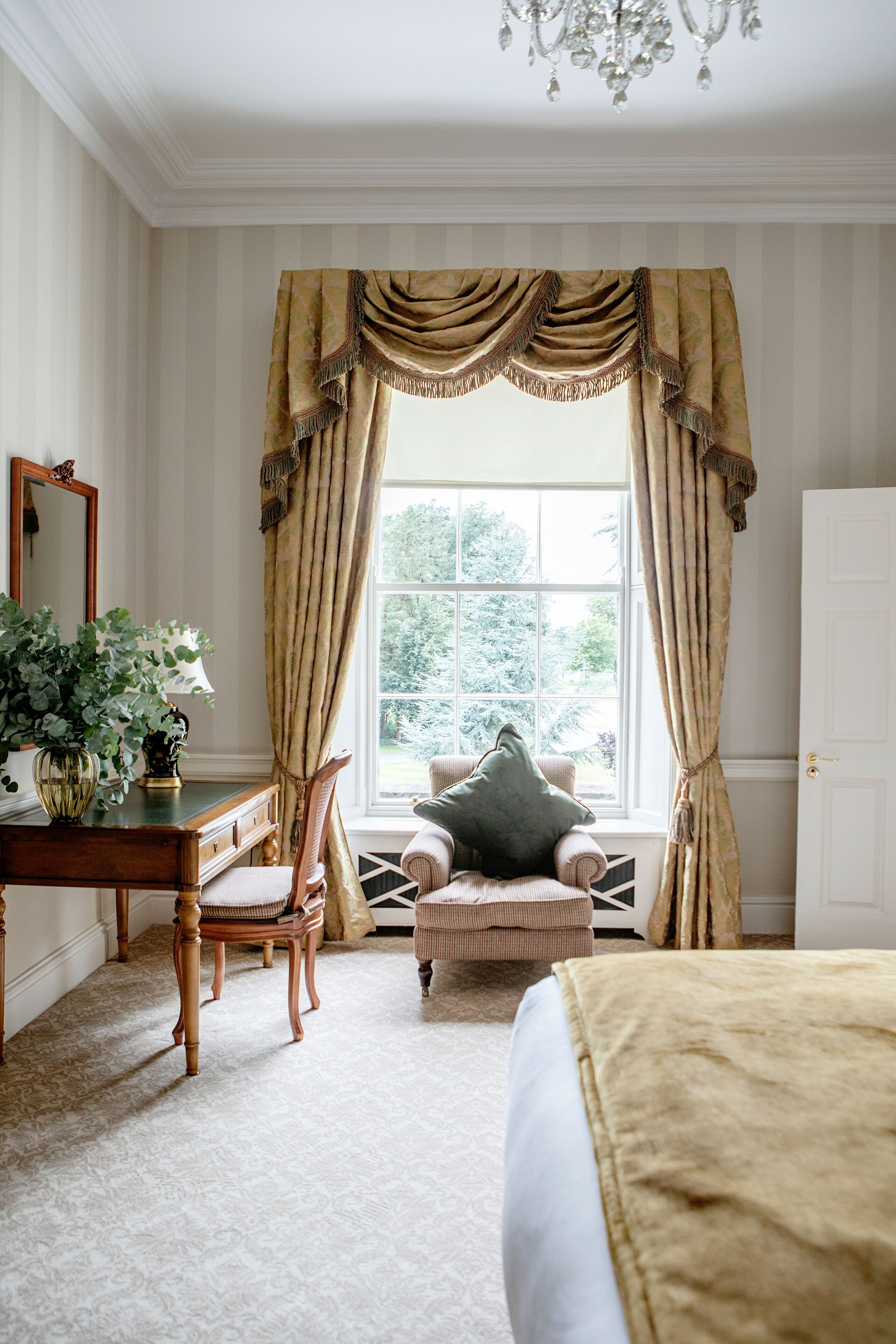 Une pièce avec une grande fenêtre, un bureau avec une lampe, une chaise, un canapé et un lit.