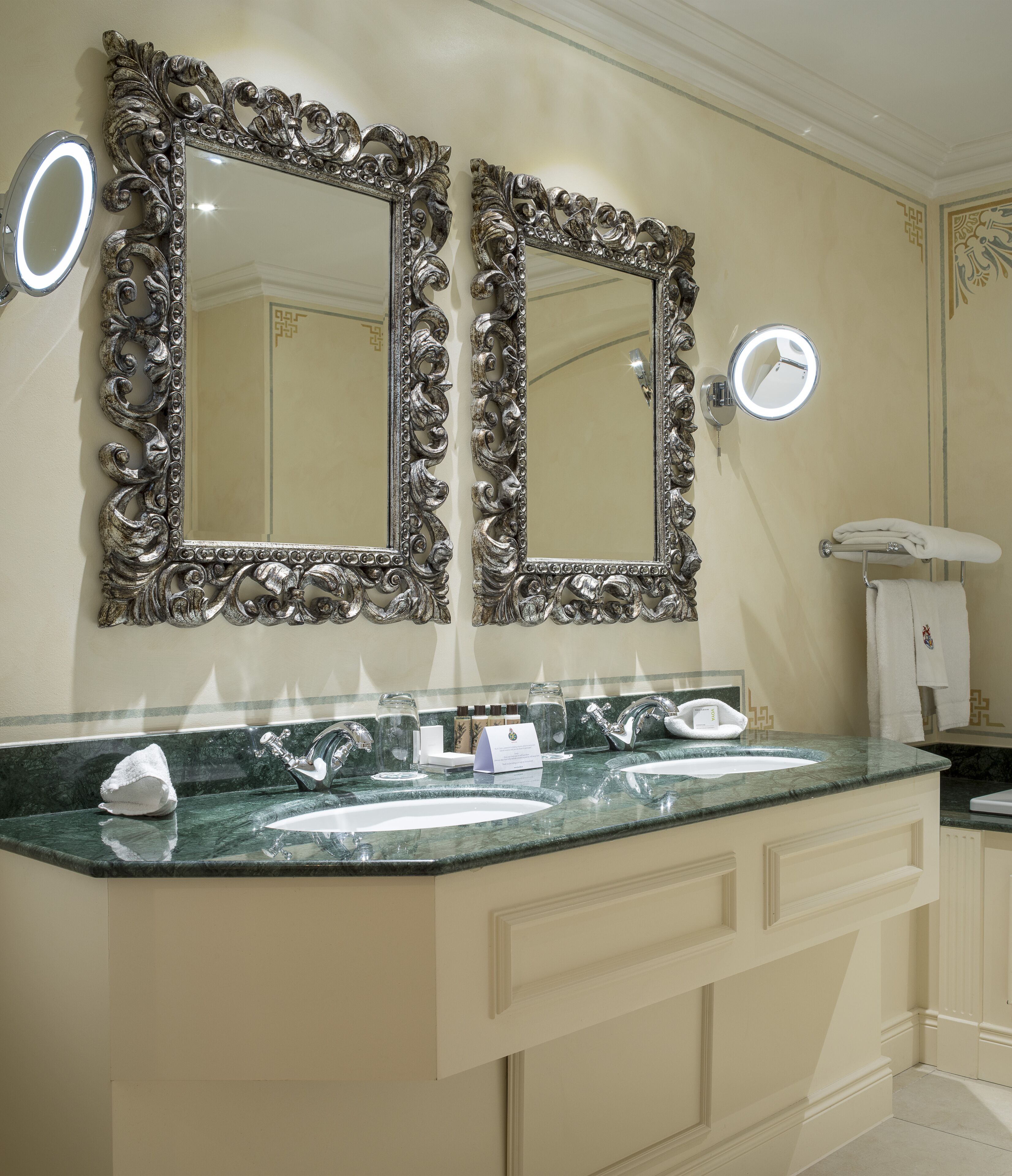 A bathroom with two ornate mirrors, a marble countertop, and a towel rack.