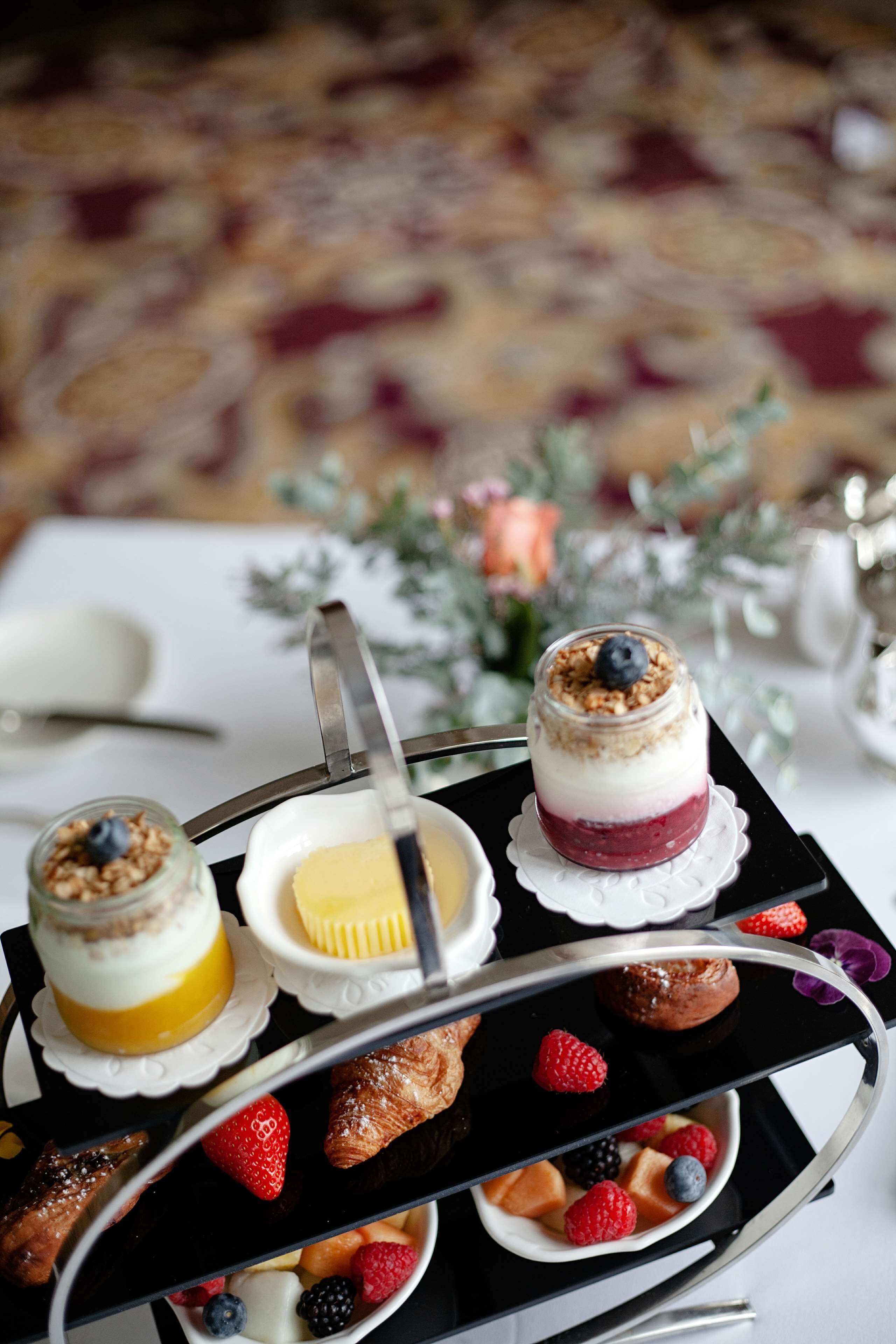 Eine Tablett mit verschiedenen Speisen, darunter ein Schichtdessert, ein Gebäckstück und frische Beeren.