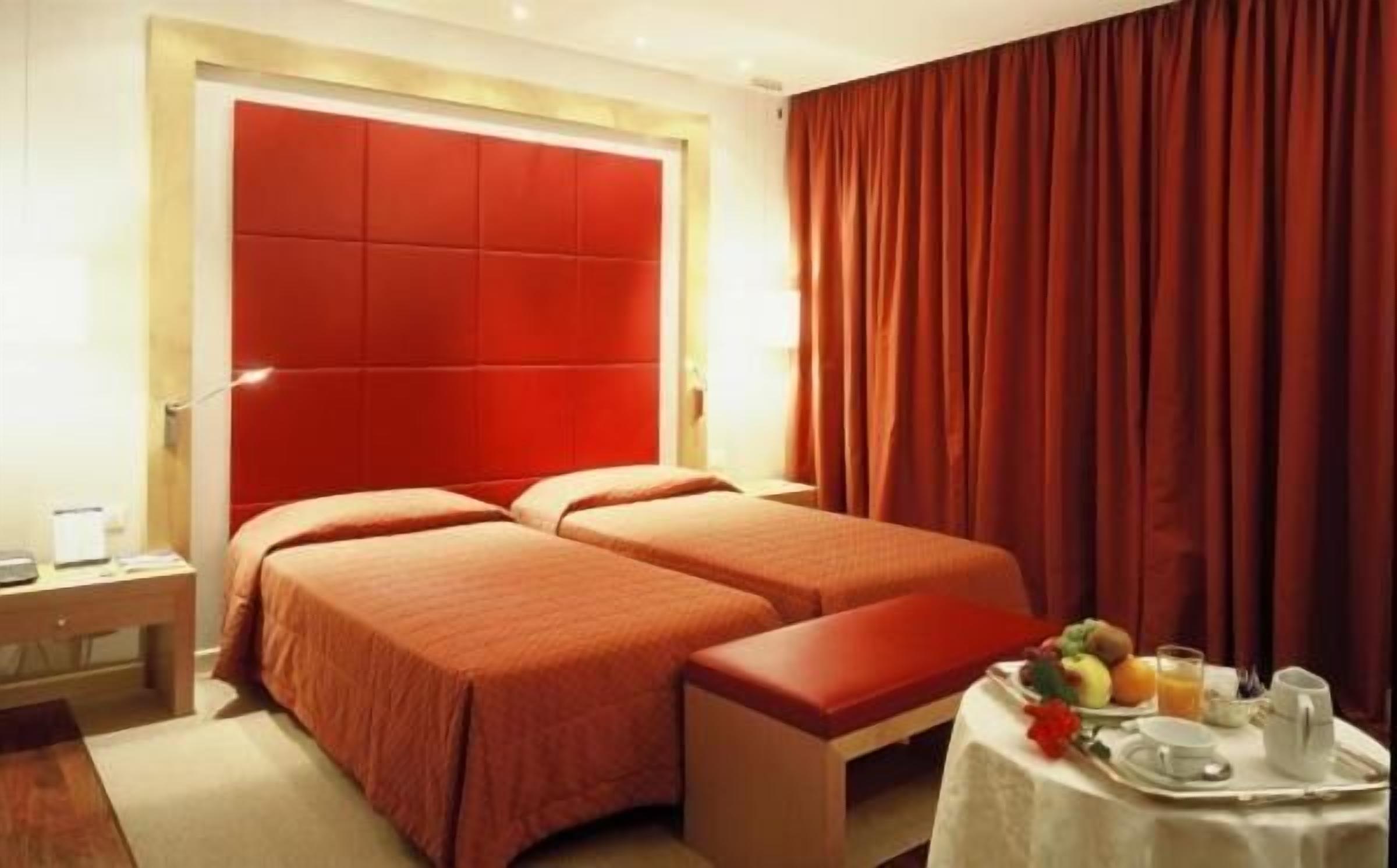 A hotel room with two beds, a small table with breakfast, and a red curtain.