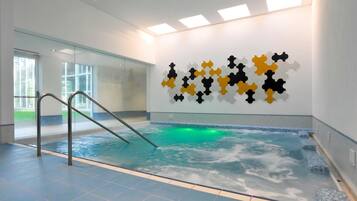 Una piscina interior con pared de vidrio, una escalera metálica e instalación de arte en la pared.