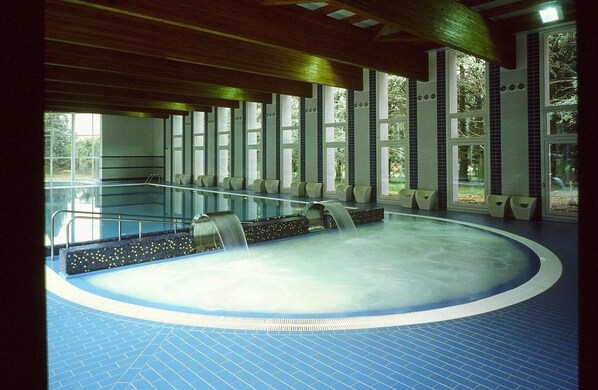 Una amplia piscina interior con suelo de baldosas y un elemento acuático central.