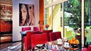 A modern dining area with red chairs, a glass table, and a large window offering a view of greenery. - Hotel delle Rose Terme & Wellnes Spa (Montechiarugolo)