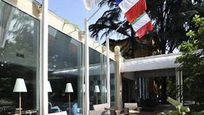 A modern outdoor seating area with wicker furniture and lamps, large windows, and flags. - Hotel delle Rose Terme & Wellnes Spa (Montechiarugolo)
