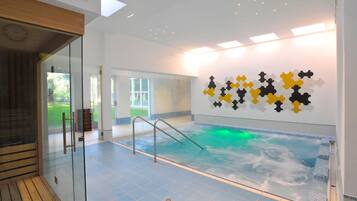 An indoor swimming pool with glass walls, a wooden deck, and a wall art installation.