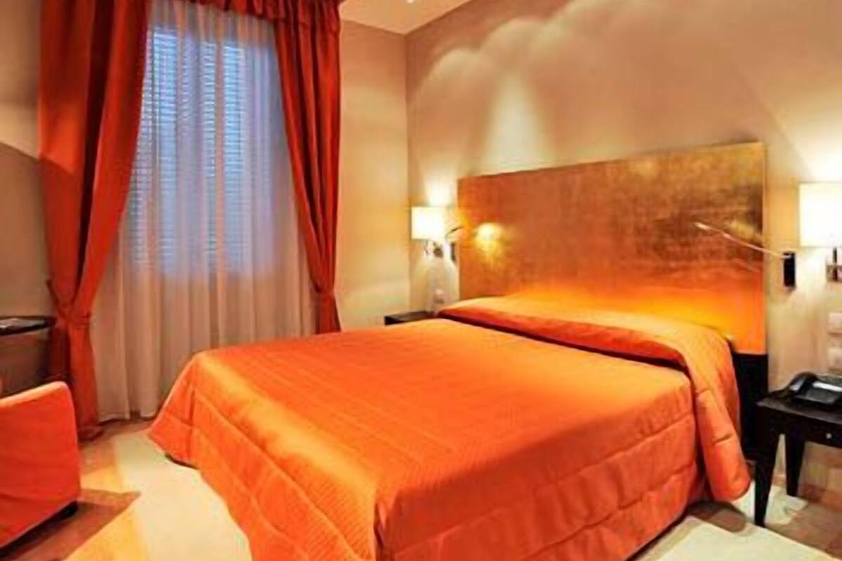 Ein Hotelzimmer mit einem großen Bett, zwei Nachttischen, einem Fenster mit Vorhängen.