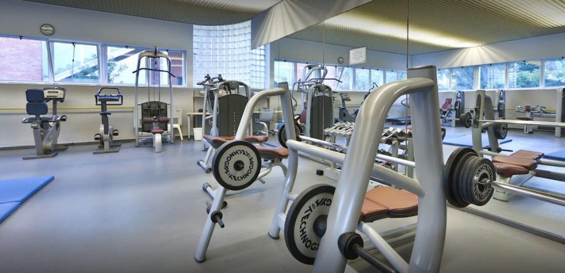 Una palestra con diverse macchine per esercizi, ampie finestre e un design moderno e pulito.