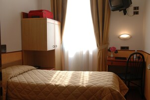 Hotelkamer met een bed, een bureau met stoel, een aan de muur bevestigde televisie en een raam met gordijnen.