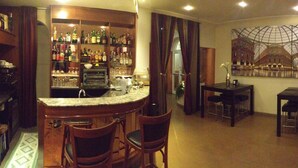 A bar area with a marble countertop and multiple stools, a dining area with a table and chairs, and a large mural of a building on the wall. - Hotel Aspromonte (Milan)