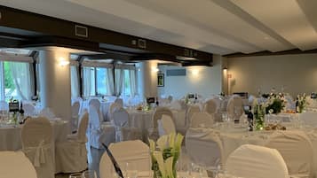 Une salle de banquet avec des tables rondes dressées pour un événement formel, agrémentée de nappes blanches, de verres et de compositions florales.