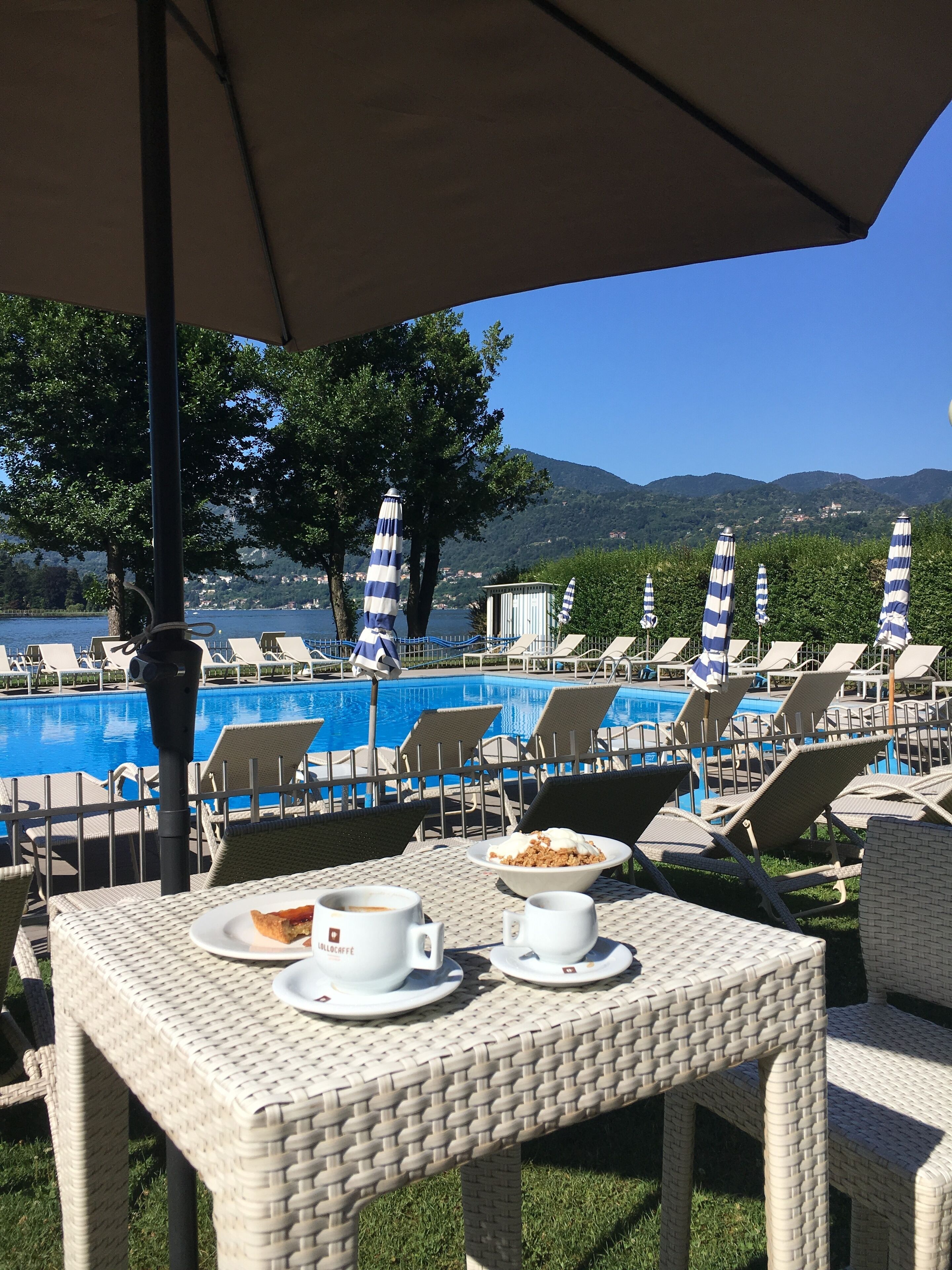 A poolside area with lounge chairs and umbrellas, overlooking a pool and a mountainous landscape.