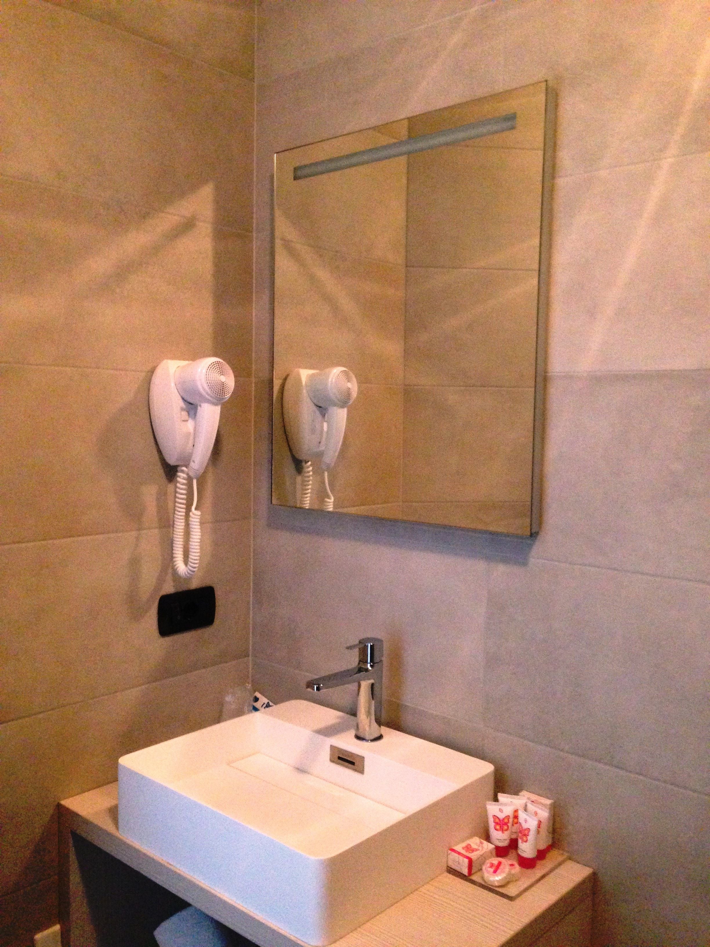 A bathroom with a white sink, a mirror, and two hair dryers mounted on the wall.