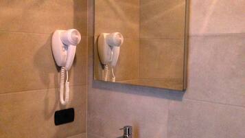 A bathroom with a white sink, a mirror, and two hair dryers mounted on the wall.