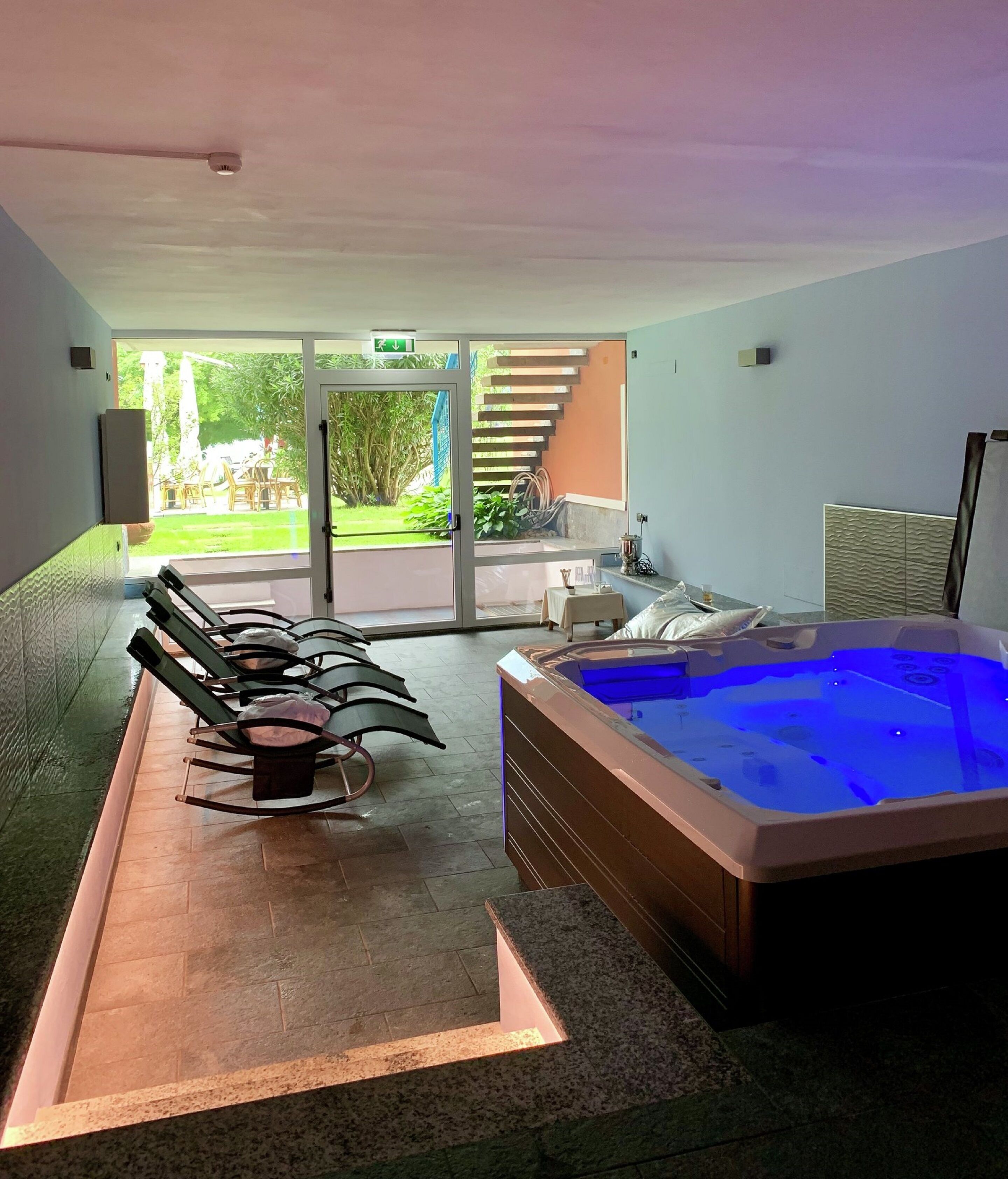 Un espace spa comprenant un jacuzzi, des chaises longues et une vue sur le jardin, accessible par des portes vitrées.