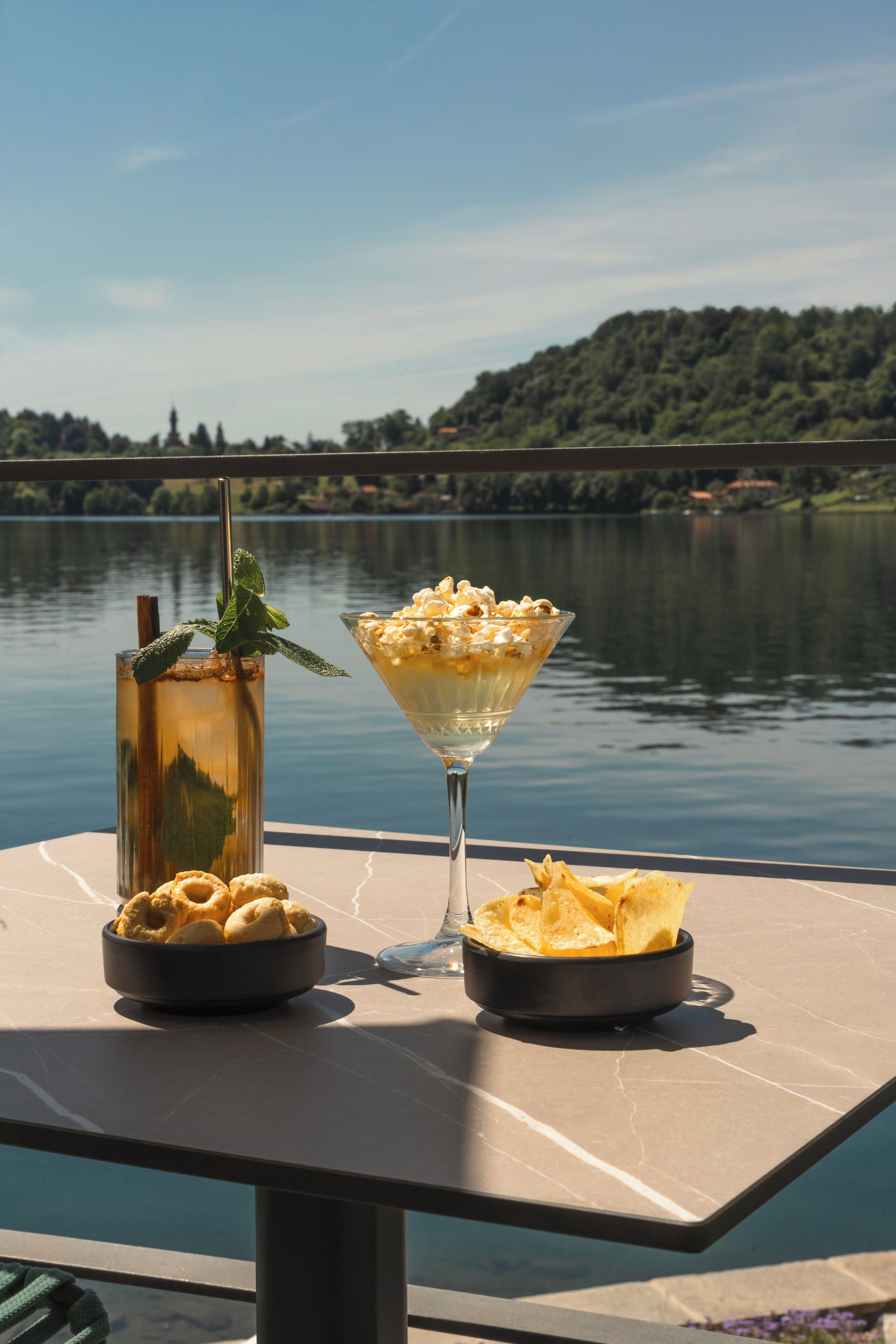 Een tafel met een drankje, popcorn en chips, met uitzicht op een meer.