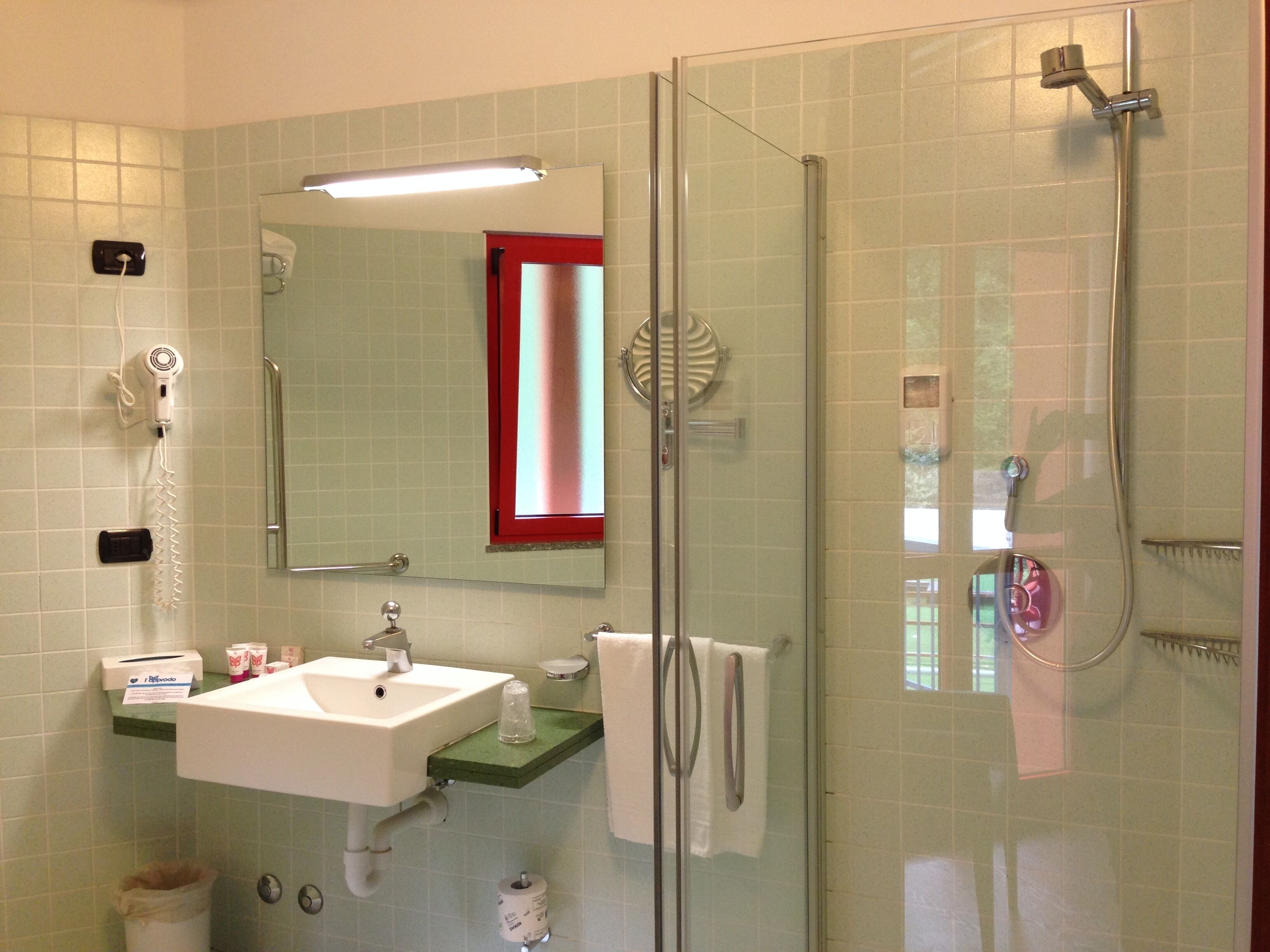 Een badkamer met een douchecabine van glas, een wastafel met spiegel erboven en een handdoekrek.