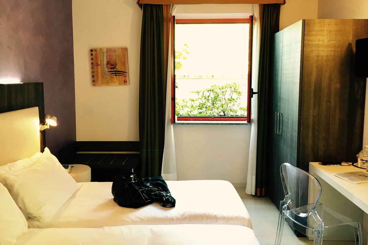 Une chambre d’hôtel comprenant un lit, un bureau, une chaise, une fenêtre avec des rideaux, un tableau au mur et un téléviseur.