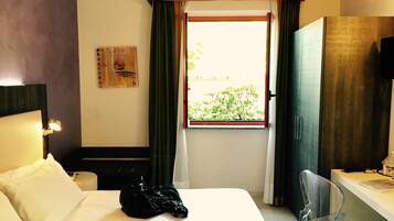Hotelkamer met een bed, bureau, stoel, raam met gordijnen, schilderij aan de muur en een televisie.