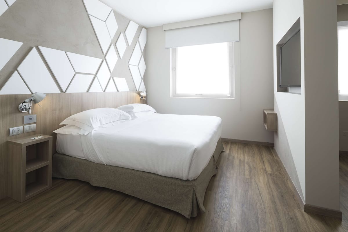 Un dormitorio moderno con cama, mesita de noche, lámpara y ventana.