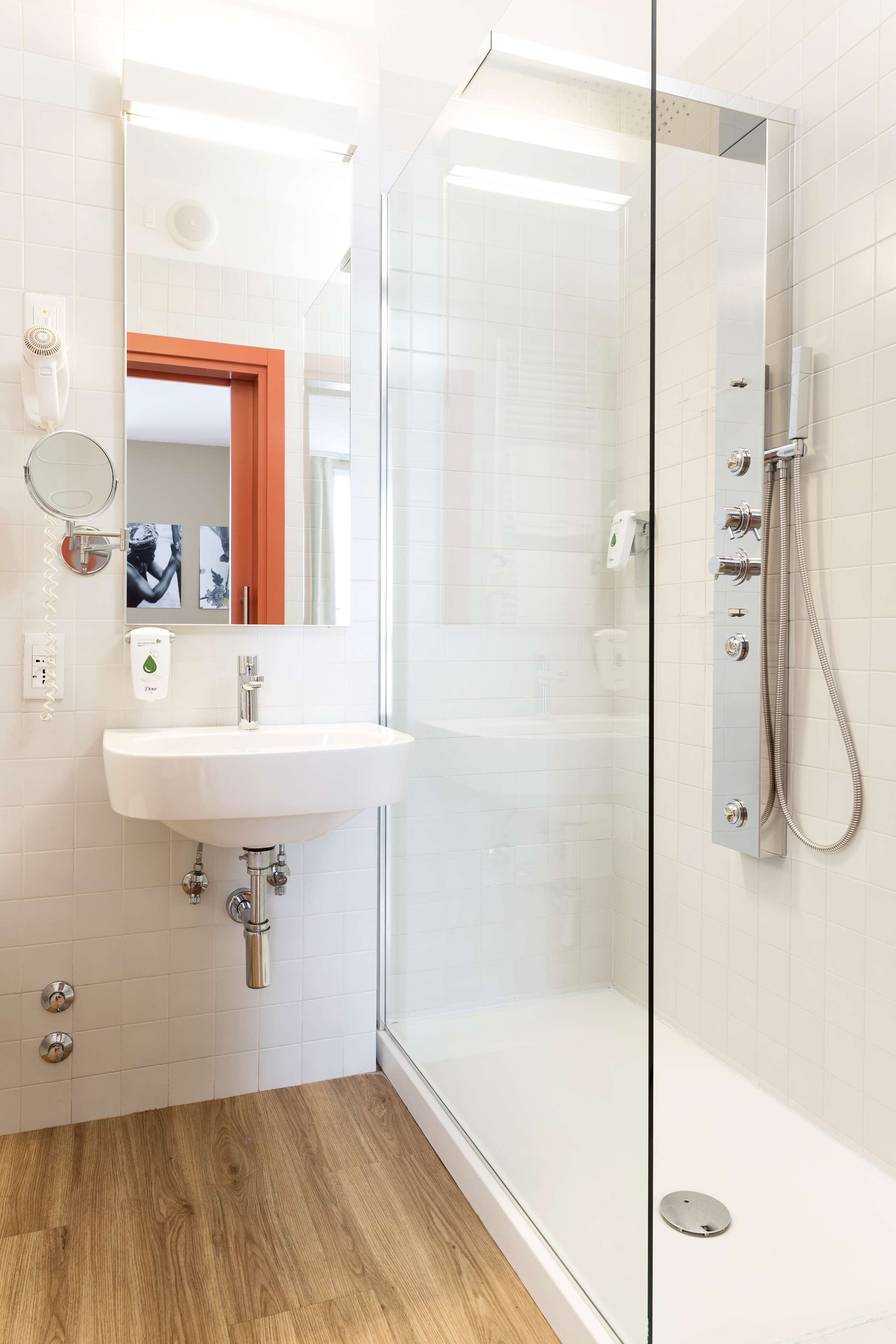 A modern bathroom with a glass-enclosed shower, a white sink, and a wooden floor.