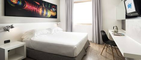 A hotel room with a bed, a desk, a TV, and a painting on the wall.