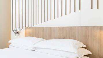 A hotel room with a wooden headboard, white bedding, and a wall-mounted lamp.