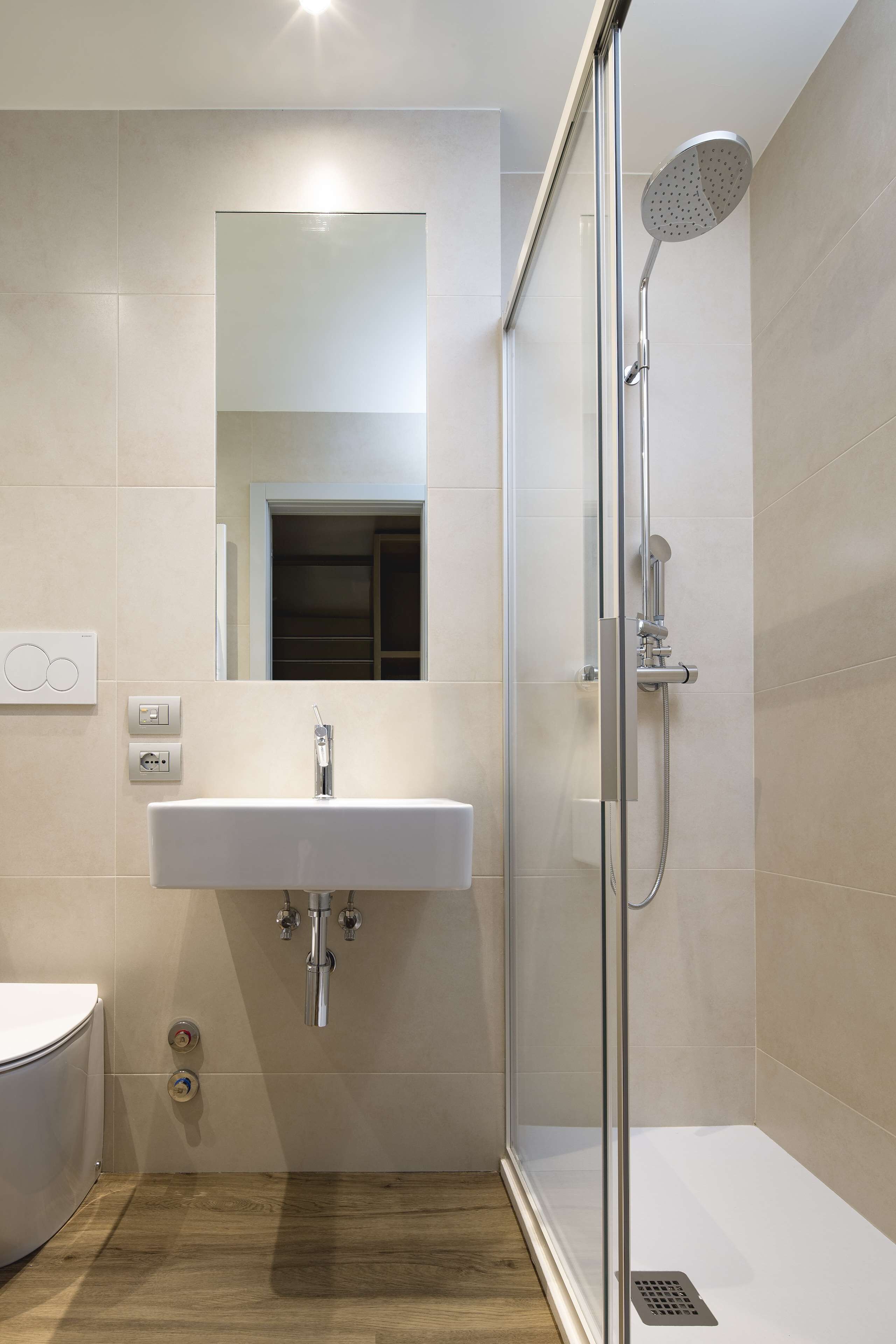 Une salle de bain moderne avec une douche à parois de verre, un lavabo blanc avec un miroir au-dessus, et un plancher en bois.