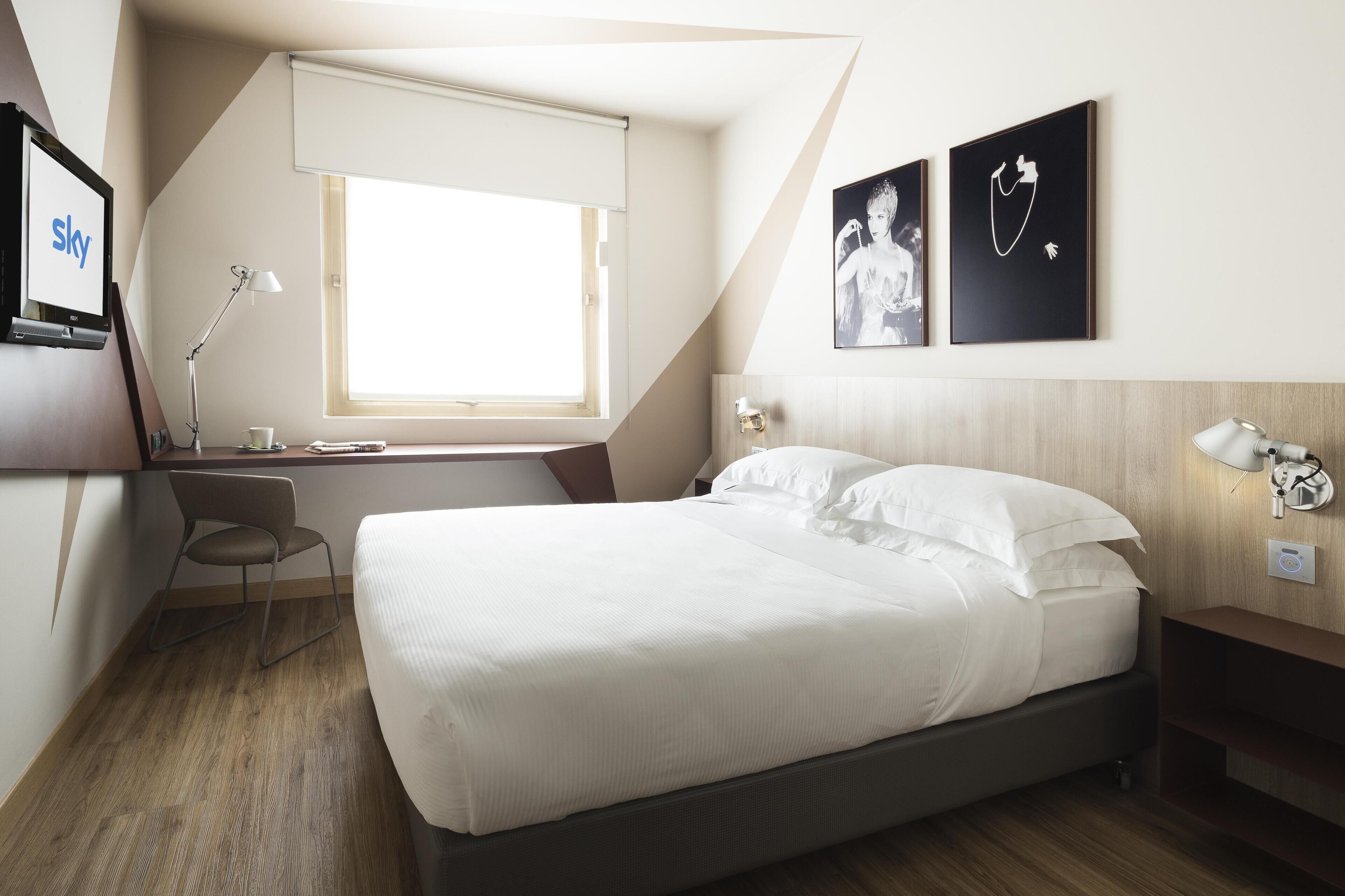 Une chambre d’hôtel moderne, équipée d’un lit, d’un bureau, d’une chaise et ornée d’œuvres d’art sur les murs.