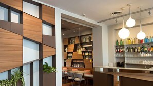 Un bar moderno con paneles de madera, una zona de estar con mesas y sillas, y una estantería llena de libros y objetos decorativos.