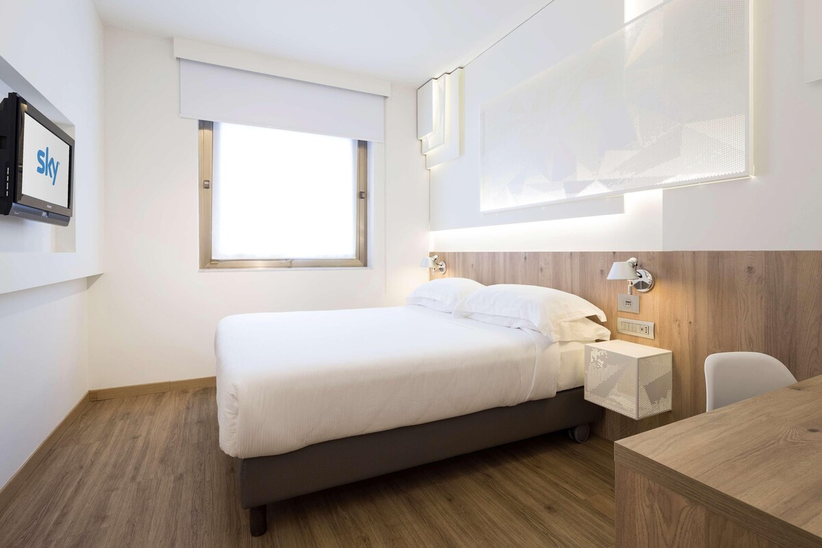 Una habitación de hotel moderna con cama, mesita de noche y escritorio.