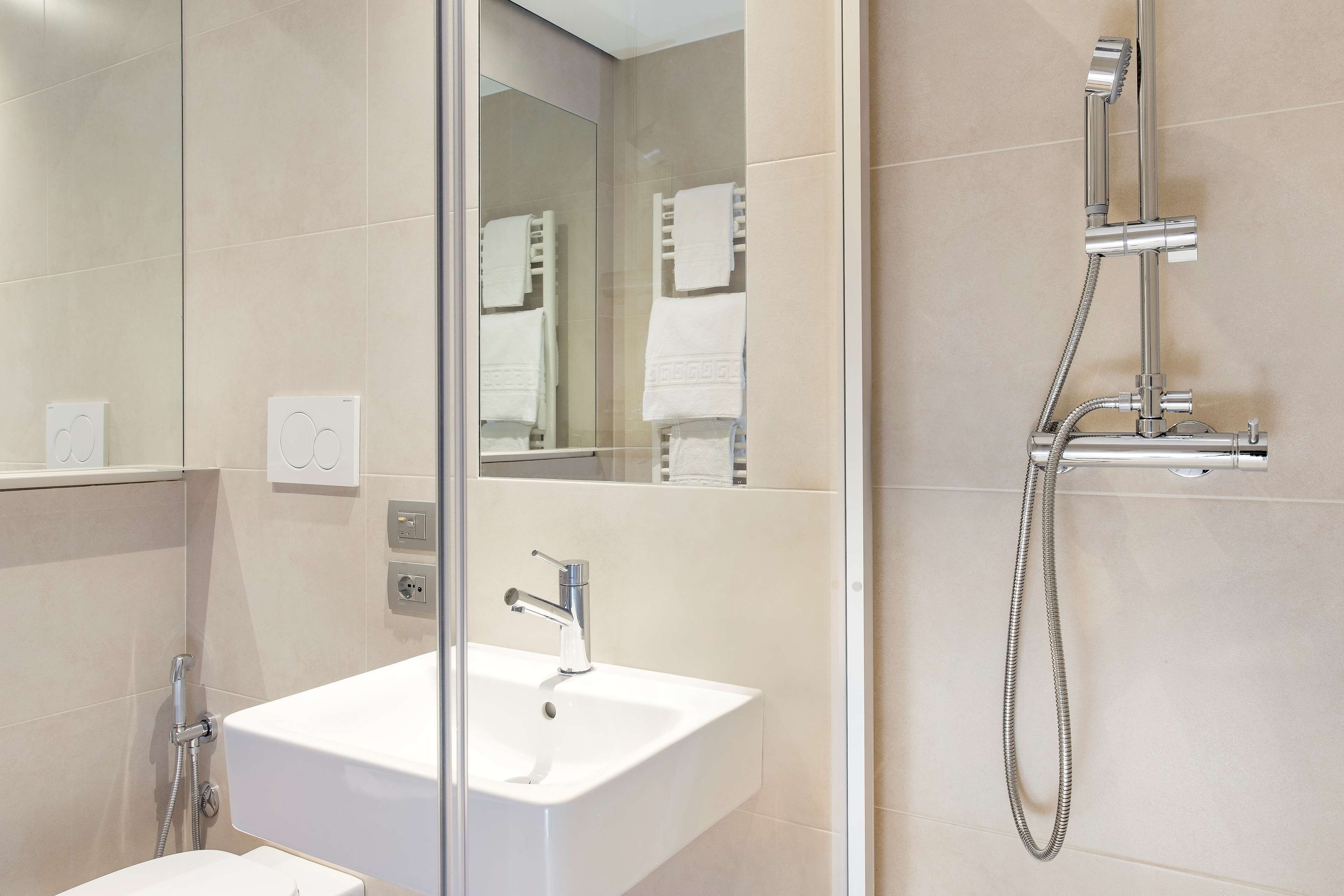 Un baño moderno con un lavabo blanco, un espejo y una ducha con cabezal de ducha manual.