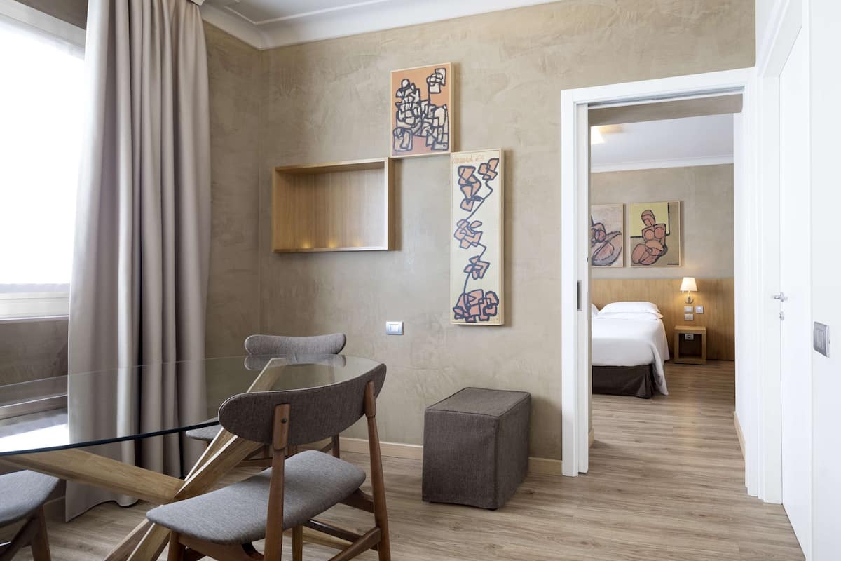 Habitación de hotel con zona de comedor, cama, obras de arte en las paredes y vistas a la ciudad.