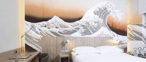 Habitación de hotel con cama, escritorio, silla y un mural en la pared con un diseño de ola.