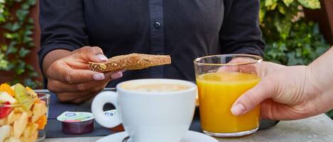 Henkilö istuu pöydän ääressä, ja hänen edessään on kahvikuppi ja kulho täynnä hedelmäsalaattia. Hänellä on kädessään viipale paahtoleipää ja lasi appelsiinimehua.