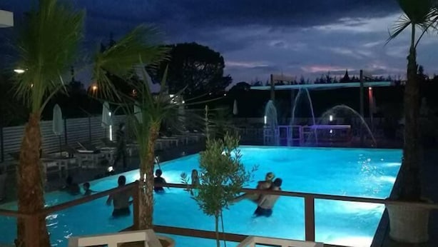 Área de piscina com vista para o céu, cercada por cadeiras brancas e palmeiras.