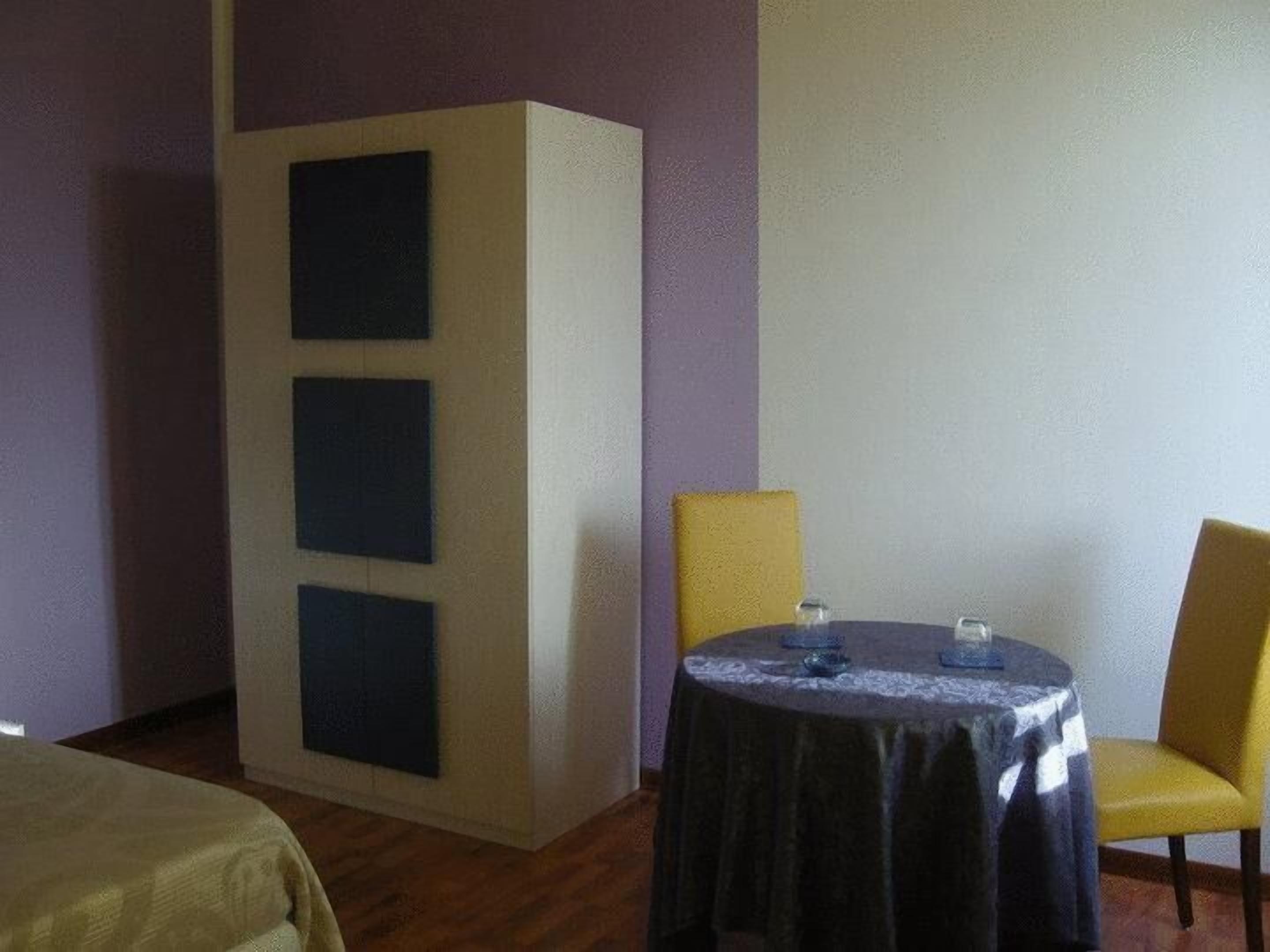 A room with a bed, a table with a tablecloth, and two chairs.