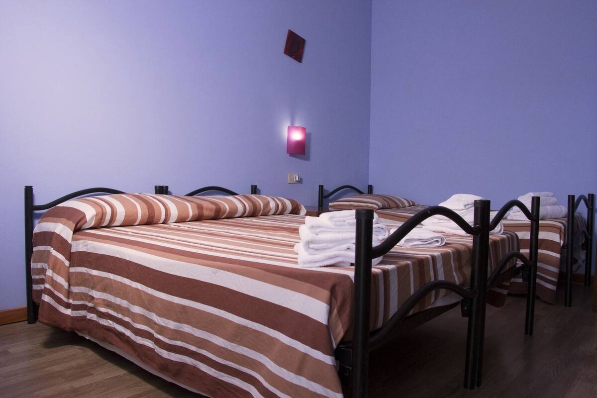 Hotellihuone, jossa on kaksi sänkyä. Kummassakin sängyssä on raidallinen vuodevaatesetti ja mustat metalliset sängynrungot.