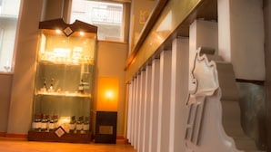 Corredor de hotel com uma vitrine de garrafas de vinho, uma escadaria de design singular e iluminação interna acolhedora.
