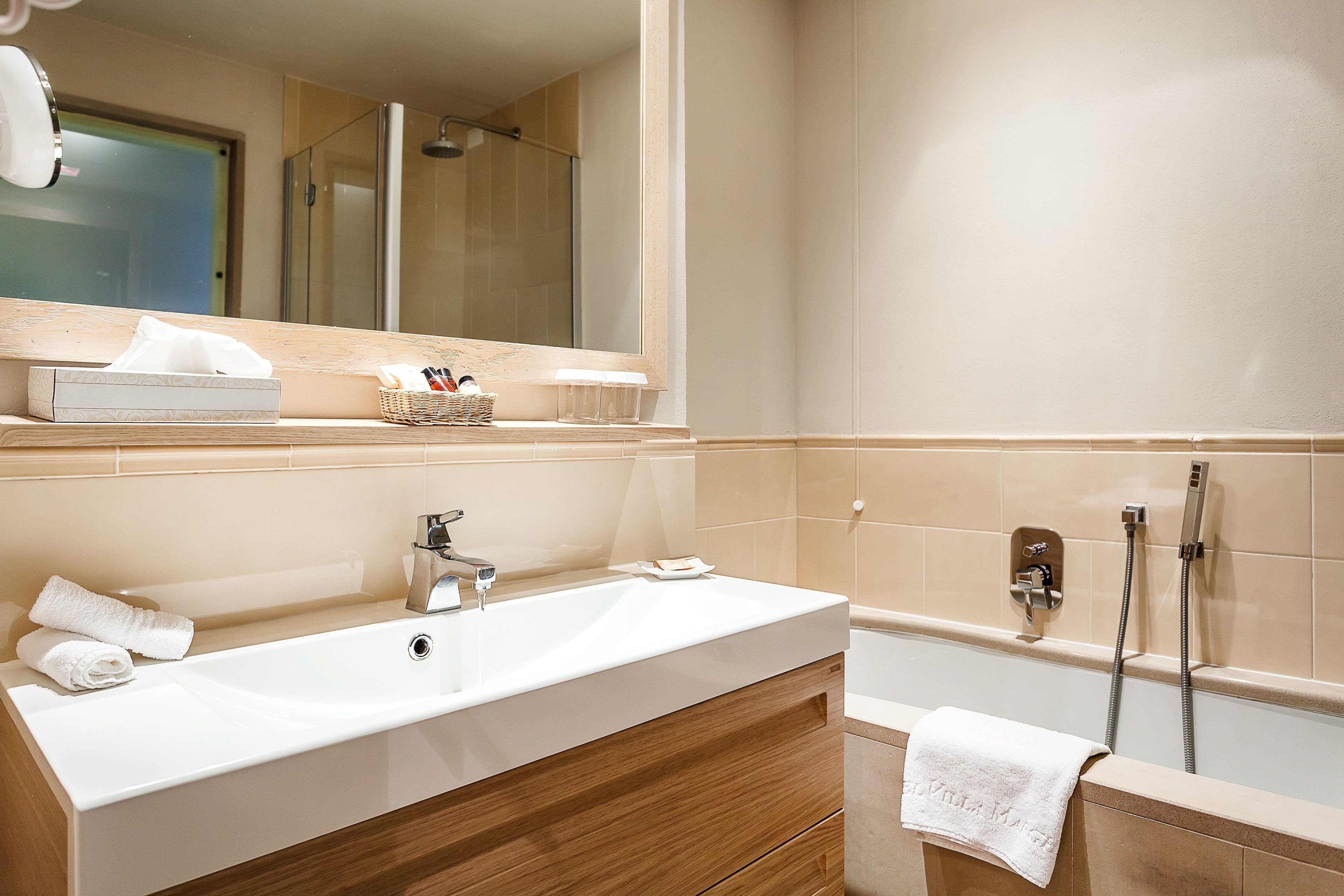 A modern bathroom with a large sink, a mirror, a shower area, and a wooden vanity.