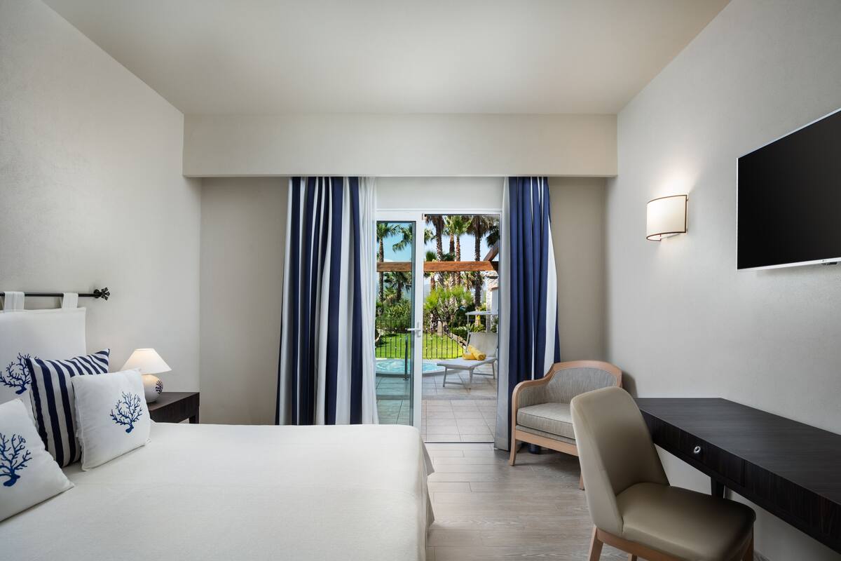 Une chambre d’hôtel équipée d’un lit, d’un bureau, d’une chaise, d’une télévision et offrant une vue sur l’espace extérieur.