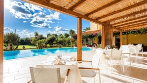 Un espace extérieur aménagé pour les repas, avec des tables et des chaises, une piscine et une vue sur un jardin paysager.