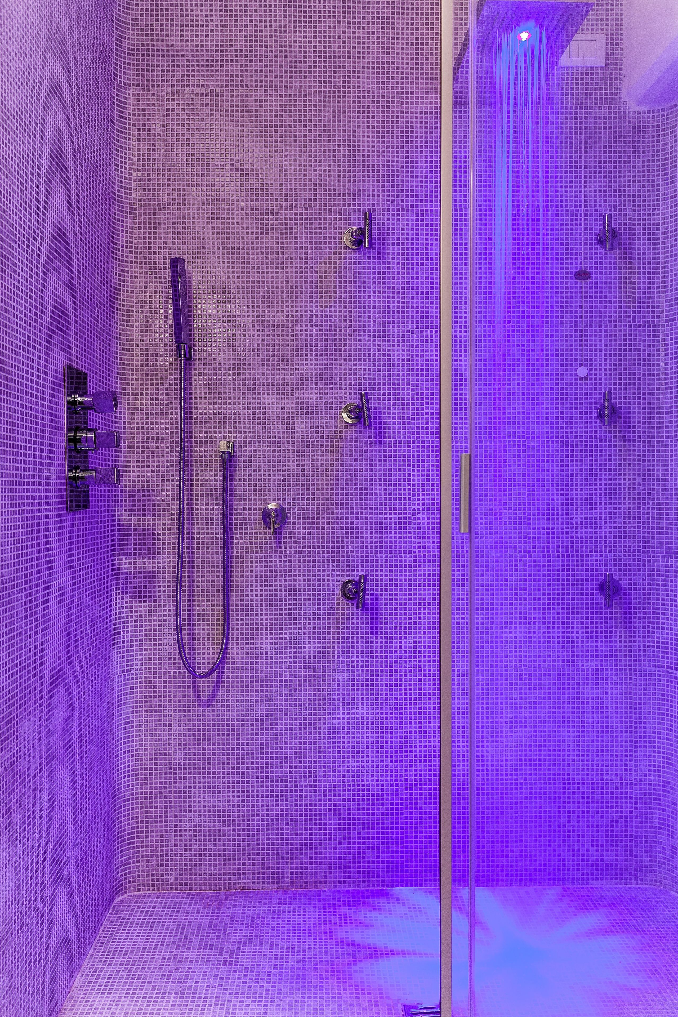 A bathroom with a tiled wall, a showerhead, and a handheld shower attachment.